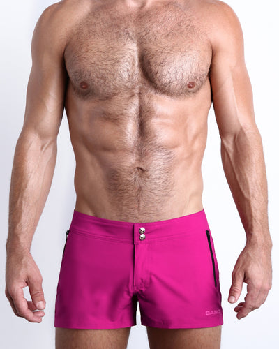 Frontal view of male model wearing the CONFESS MAGENTA men’s beach shorts in a solid bright magenta color by the Bang! brand of men's beachwear from Miami.