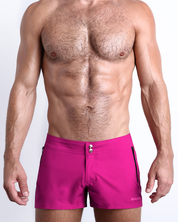 Frontal view of male model wearing the CONFESS MAGENTA men’s beach shorts in a solid bright magenta color by the Bang! brand of men&