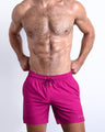 Frontal view of sexy model wearing the CONFESS MAGENTA men’s all-purpose swimwear bottoms in a solid bright magenta pink color by the Bang! brand of men's beachwear from Miami.