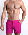 Frontal view of a sexy male model wearing the men’s CONFESS MAGENTA beach tailored shorts in a solid bright magenta color by the Bang! Menswear brand from Miami.