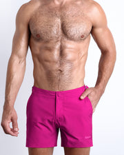 Frontal view of a sexy male model wearing the men’s CONFESS MAGENTA beach tailored shorts in a solid bright magenta color by the Bang! Menswear brand from Miami.