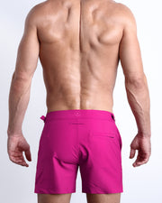 Back view of a male model wearing the CONFESS MAGENTA Tailored Shorts men’s beach shorts in a bright pink color by the Bang! Clothes brand of men's beachwear.