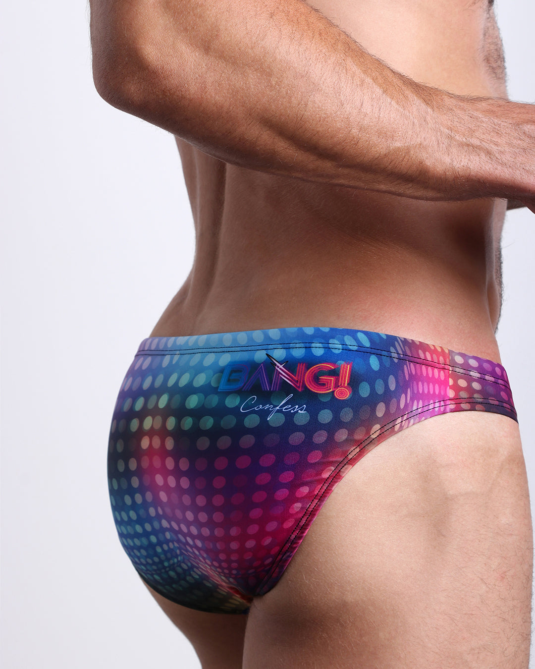 Back view of model wearing CONFESSIONS ON A SAND FLOOR men’s beach mini-brief in a multi color disco ball inspired by Madonna, Abba, and Studio 54 and showing the BANG! Confess logo made by the Bang! Miami official brand of men's swimwear.