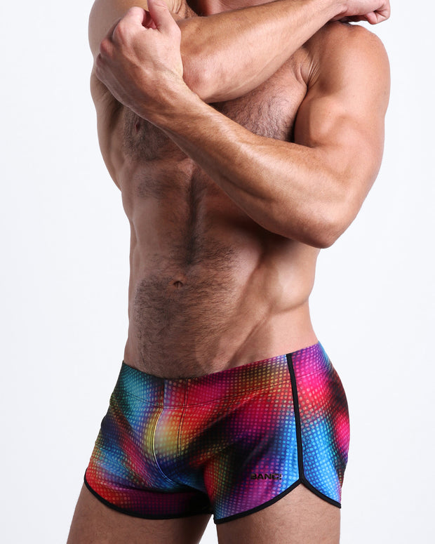 Side view of muscular male model wearing CONFESSIONS ON A SAND FLOOR Summer swimsuit for the beach featuring a pop color disco ball print by BANG! Miami.