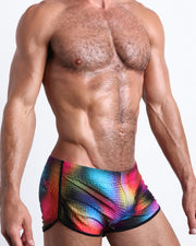 Side view of muscular male model wearing CONFESSIONS ON A SAND FLOOR Summer swimsuit for the beach featuring a pop color disco ball print by BANG! Miami.