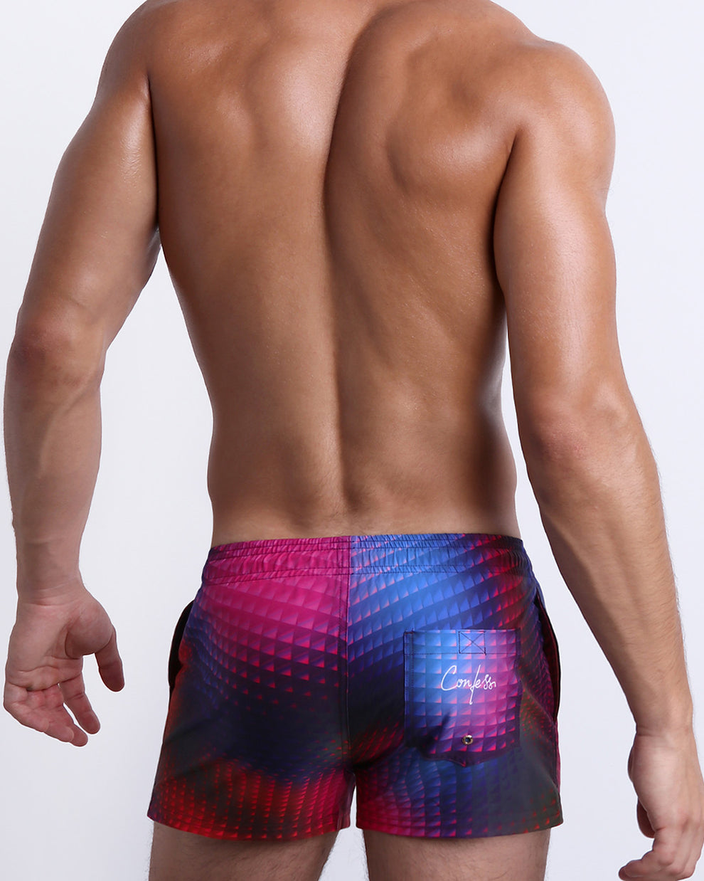 Back view of a male model wearing men’s CONFESSIONS ON A SAND FLR VOL 2 beach shorter leg length Show Shorts in a pop color with disco ball print and a back pocket with the phrase "Confess" made by BANG! Clothes in Miami.