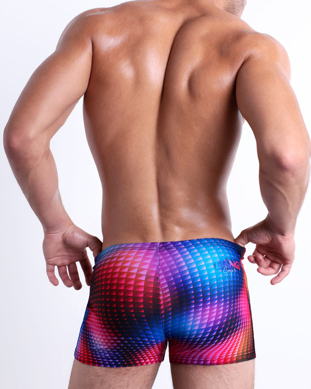 Back view of a model wearing CONFESSIONS ON A SAND FLR VOL 2 men’s beach sexy Swim Trunks featuring a multi color disco ball inspired by Madonna, Abba, and Studio 54 and showing th BANG! Confess logo, designed by BANG! Clothes in Miami.