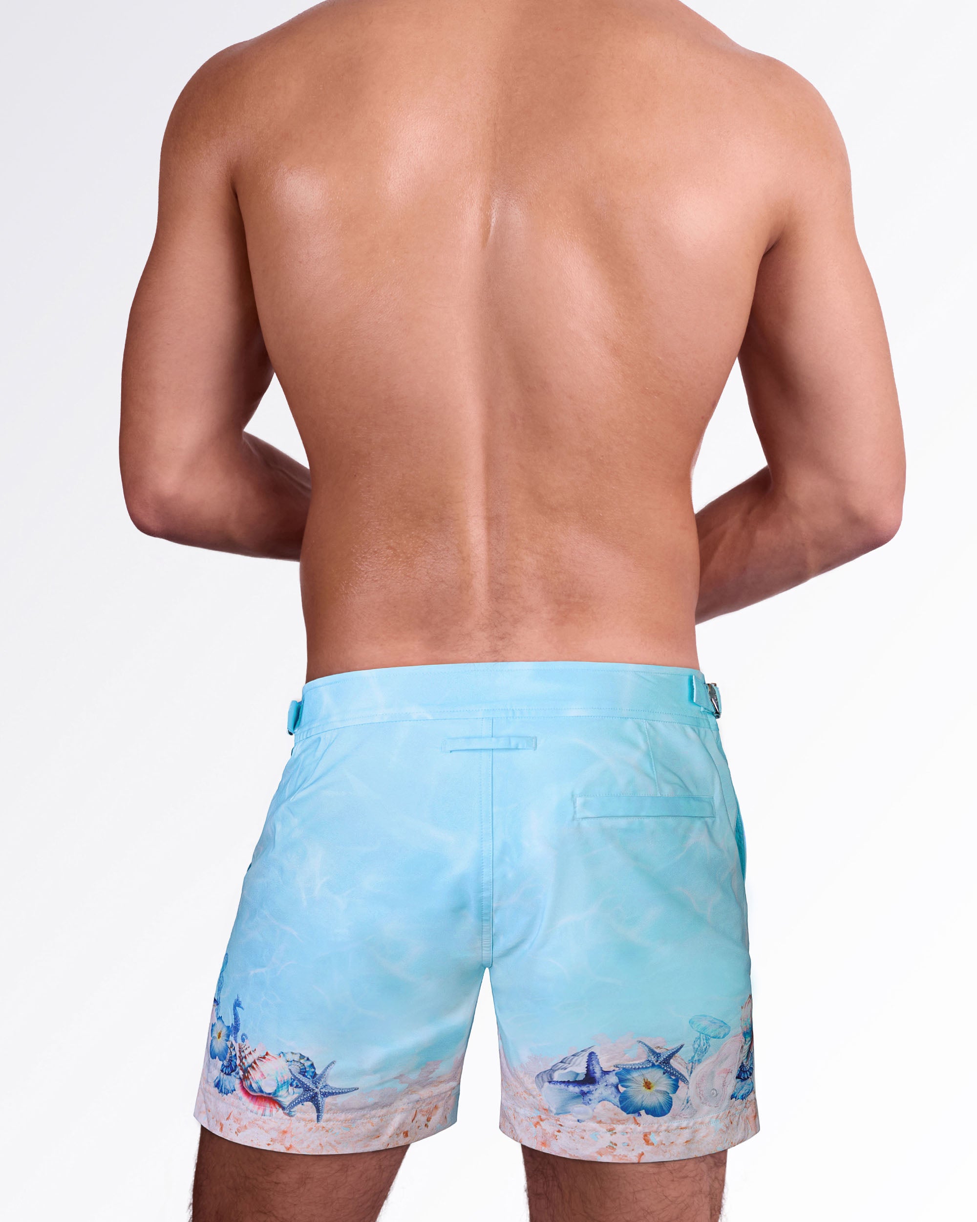 Back view of Coral Way Tailored Shorts featuring a soft blue water print, coastal shell artwork, and tailored swim short design.