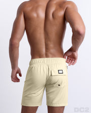 Back view of male model wearing men’s CREAM FIELDS beach Flex Boardshorts swimming shorts in a solid light pale yellow color, complete the back pockets, made by DC2 a capsule brand by BANG! Clothes in Miami.