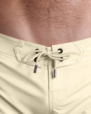 Close-up view of inseam and details of CREAM FIELDS beach shorts for men, with a beige color cord and custom branded silver cord-ends, and matching custom eyelet trims in black. 