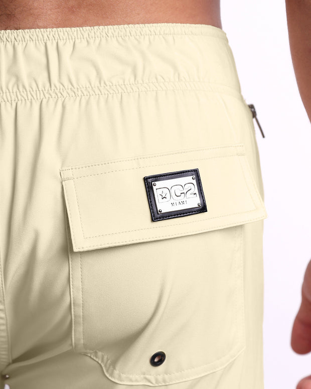 Close-up view of the CREAM FIELDS men’s Flex Boardshorts back pocket, showing custom branded silver metal logo.
