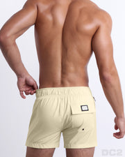 Back view of a male model wearing men’s CREAM FIELDS Flex Shorts swimsuits in a solid light yellow color, complete the back pockets, made by DC2 a capsule brand by BANG! Clothes in Miami.