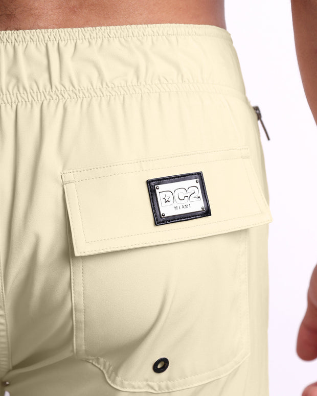 Close-up view of the CREAM FIELDS men’s Flex Shorts back pocket, showing custom branded silver metal logo.