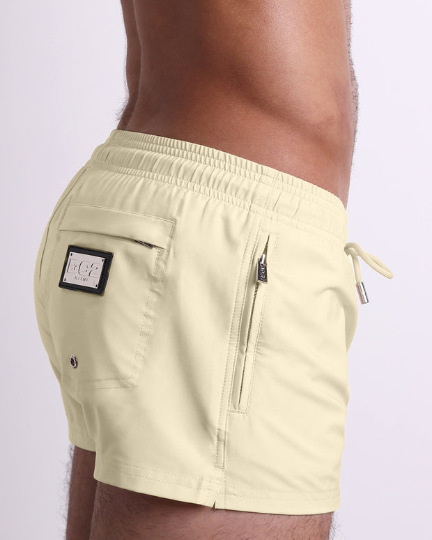 Side view of the CREAM FIELDS swimsuit Poolside Shorts men’s shorter length shorts with side zipper pocket featuring a light tan color. These high-quality swimwear bottoms by DC2, a men’s beachwear brand from Miami.