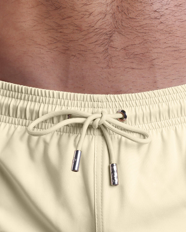 Close-up view of the CREAM FIELDS men’s summer shorts, showing a beige cord with custom branded silver cord ends, and matching custom eyelet trims in silver.