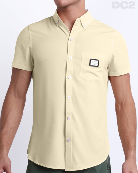 This is a front view of a male model looking sexy in a CREAM FIELDS stretch shirt for men. The shirt is a solid pale beige color on the left pocket. It's a premium quality button-up top made by DC2, a Miami-based men's beachwear brand.