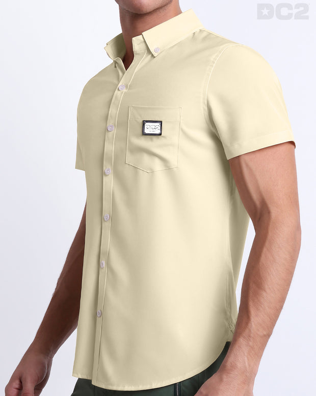 Side view of a masculine model wearing the men’s CREAM FIELDS Summer button-down shirt in a solid light tan color. This high-quality shirt is by DC2, a men’s beachwear brand from Miami.