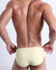 Back view of male model wearing the CREAM FIELDS beach briefs for men by BANG! Miami in a solid pastel yellow color.