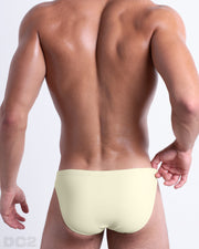 Back view of male model wearing the CREAM FIELDS beach mini-briefs for men by BANG! Miami in a solid light cream color.