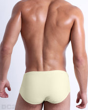 Back view of male model wearing the CREAM FIELDS beach Brazilian Sunga swimwear for men by BANG! Miami in a solid light yellow color.