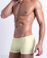 Side view of a masculine model wearing men’s swimsuit compression shorts in a light pastel yellow color featuring a side pocket with official logo of DC2 Brand.