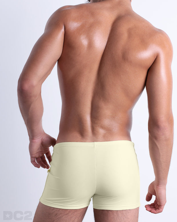 Back view of a male model wearing the CREAM FIELDS men’s swim trunks by BANG! Miami in a solid pale yellow color.
