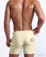 Male model wearing men’s CREAM FIELDS Summer Tailored Shorts swimsuit in a solid light yellow color, complete with a back zippered pocket, designed by DC2 a BANG! Clothes capsule brand in Miami.
