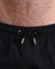 Close-up view of the DARK KNIGHT men’s summer shorts, showing dark black cord with custom branded golden cord ends, and matching custom eyelet trims in gold.