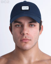 A man wearing the NAVY BLUE - Chillax Cap, a stylish blue color baseball cap made from breathable fabric. The cap features a metallic silver logo plaque on the front and a curved brim for sun protection.