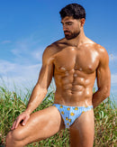 BANG Ducks Just Wanna Have Fun Swim Mini Brief — model wearing blue striped men’s swim mini brief with yellow duck print outdoors.