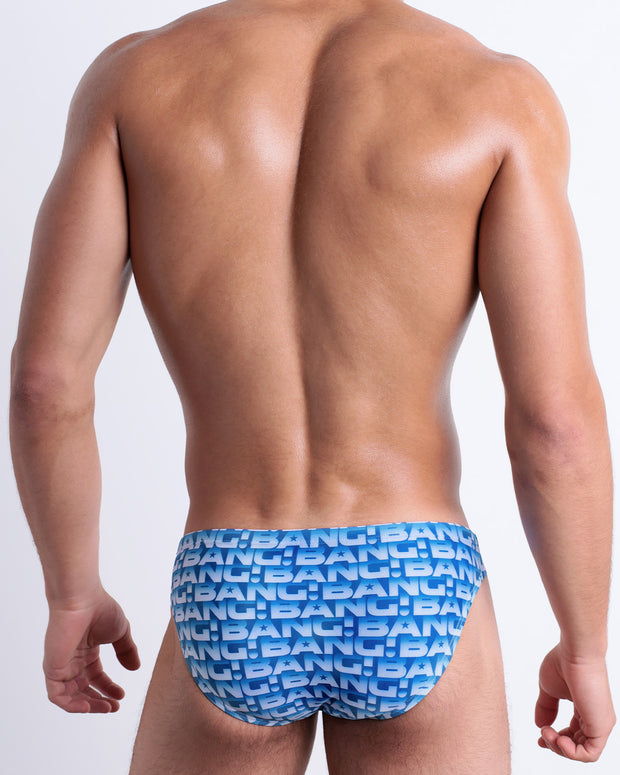 Back view of a model wearing ESCAPADE (BLUE/WHITE) men’s beach brief features a blue and white monogram design, is designed by BANG! Clothes in Miami.