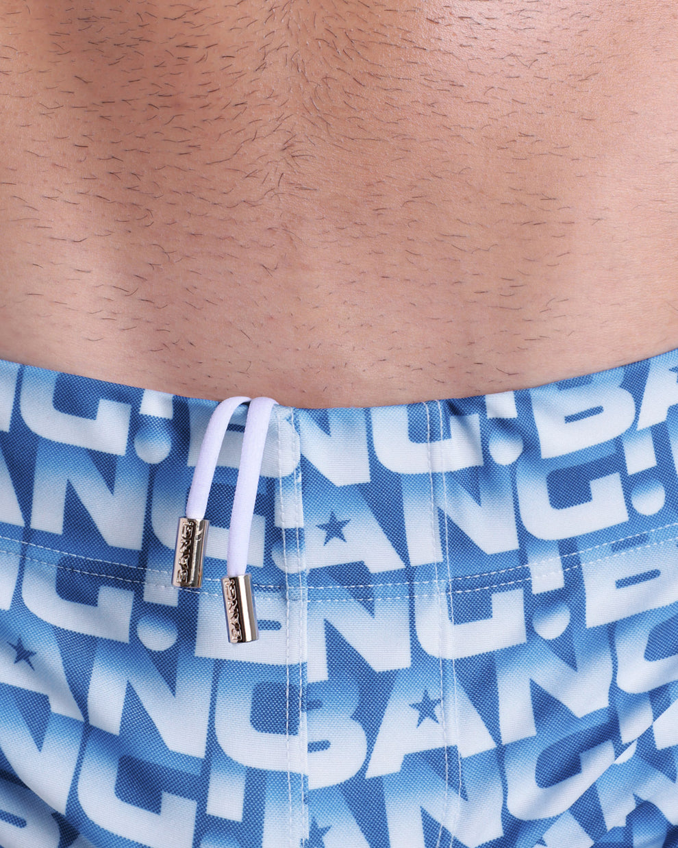 Close-up view of trims of ESCAPADE (BLUE/WHITE) waistband drawstring, with white cord and custom branded golden cord-ends, and matching custom eyelet trims in gold.