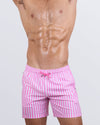 Frontal view of a male model wearing the FAST LINES (CHILL PINK) Resort Shorts for men by DC2 Miami. These above-the-knee swim shorts feature a stylish pink and white striped pattern, an elastic waistband with an adjustable drawstring, and a relaxed fit, perfect for poolside lounging, tropical vacations, and summer getaways.