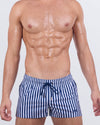 Model wearing FAST LINES (NAVY BLUE) poolside shorts in a bold navy and white vertical stripe print. Modern resortwear designed for standout beachside moments with quad-accentuating fit and metallic drawcord tips.