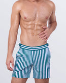 Model wearing FAST LINES (PACIFIC GREEN) tailored swim shorts for men with bold vertical stripes in green and white. High-end men’s swim trunks with a slim fit, adjustable side buckles, and quick-dry fabric. Perfect for beach days and resort fashion.