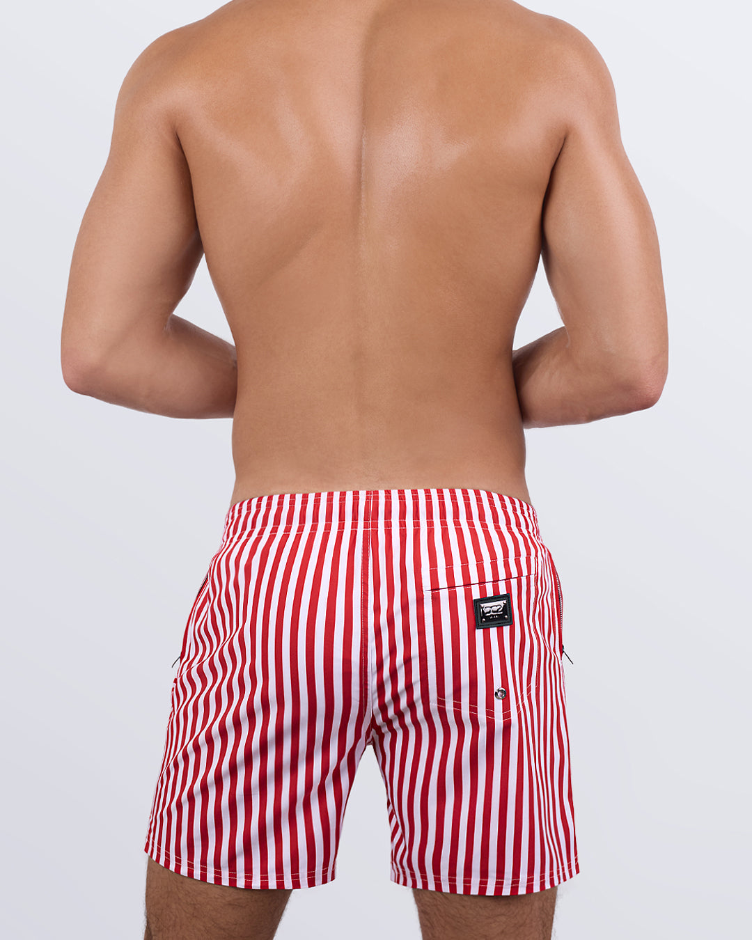 Back view of a male model wearing the FAST LINES (RAPID RED) Resort Shorts by DC2 Miami. These resort-style swim shorts showcase a tailored, long-leg cut, a functional back pocket with a DC2 signature metal logo plaque, and breathable, quick-dry fabric designed for all-day comfort.