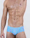 Model wearing FAST LINES (SKY BLUE) men’s swim briefs with light blue and white vertical stripes that channel a crisp, coastal vibe. This swimwear redefines the classic brief with a flattering low-rise fit and sculpted front.