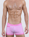 Model wearing FAST LINES (CHILL PINK) swim trunks in vertical pink-and-white stripes. Sporty square-cut silhouette with a snug fit and zippered pocket detail.