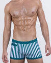 Model wearing FAST LINES (PACIFIC GREEN) men's swim trunks in green and white vertical stripes. Square-cut swimwear with contour-fit design, low-rise waistband, and signature DC2 Miami logo—perfect for beach, resort, or poolside style.