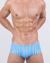 Model wearing FAST LINES (SKY BLUE) Swim Sunga – a modern Brazilian men’s swimsuit with cool sky blue and white vertical stripes. Features a snug yet comfortable fit around the waist for a confident beachside look.