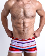 Frontal view of a sexy male model wearing men's swimsuit with mini pockets in FAWCETT SARAPE featuring the iconic Farrah Fawcett 1976 swimsuit poster print designed by the Bang! Menswear brand from Miami.