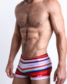 Side view of a masculine model wearing the FAWCETT SARAPE compression swimwear shorts with red and white stripes inspired by a Mexican blanket or sarape by BANG! Clothes.