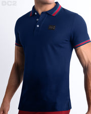 Male model wearing a slim-fitting, FONTAINE BLUE Pima Cotton Polo Shirt by Miami-based DC2. Solid dark navy blue with red and aqua green/blue stripes on ribbed-knit collar and cuffs.