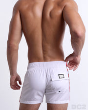 Back view of a male model wearing men’s FORZA WHITE Flex Shorts swimsuits in a solid white color with green and red side stripes, complete the back pockets, made by DC2 a capsule brand by BANG! Clothes in Miami.