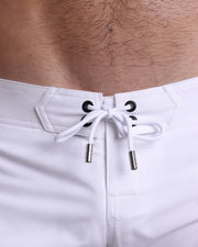 Close-up view of men’s summer Flex shorts by DC2 clothing brand, showing white color cord with custom-branded golden cord ends, and matching custom eyelet trims in gold.