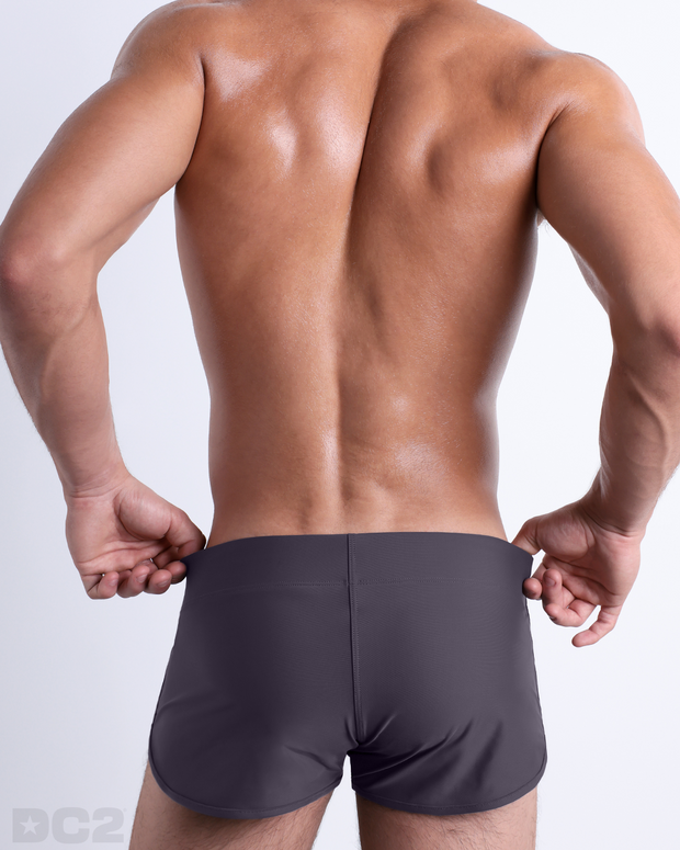Back view of male model wearing the GOTHAM GREY beach Swim Shorts for men by BANG! Miami in a solid gray color.
