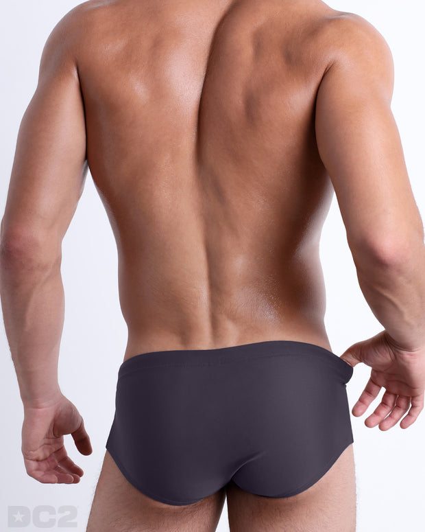 Back view of male model wearing the GOTHAM GREY beach Brazilian Sunga swimwear for men by BANG! Miami in a solid smoke gray color.