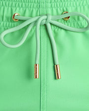 Close-up view of the GREEN PIECE men’s summer shorts, showing light green cord with custom branded golden cord ends, and matching custom eyelet trims in gold.