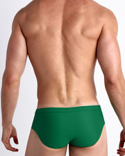 Back view of a male model wearing men’s swim briefs in GREEN RUSH a solid jade green color made with Italian-made Vita By Carvico Econyl Nylon by the Bang! Clothes brand of men's beachwear.