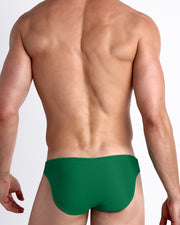 Back view of a male model wearing the GREEN RUSH beach mini-briefs made with Italian-made Vita By Carvico Econyl Nylon for men by BANG! Miami in a solid green hue.